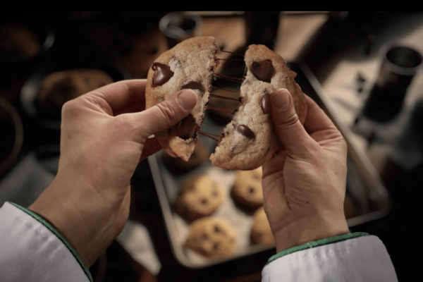 An AI-generated image of a person breaking a cookie in half with strands of chocolate hanging in the middle.